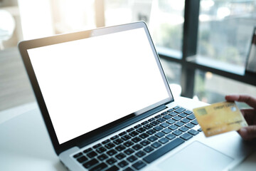 Mockup image of a businesswoman using laptop and holding credit card with blank white desktop screen with coffee cup on wooden table in cafe.