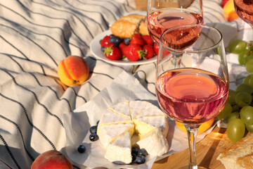 Fototapeta na wymiar Glasses of delicious rose wine and food on white picnic blanket, closeup