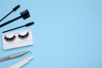 Flat lay composition with fake eyelashes on light blue background, space for text