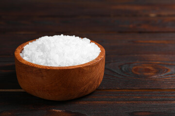 Bowl with natural sea salt on wooden table. Space for text