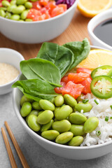 Poke bowl with salmon, edamame beans and rice on light grey table, closeup