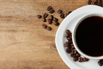 Cup of hot aromatic coffee and roasted beans on wooden table, flat lay. Space for text