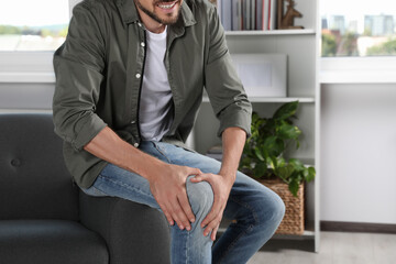 Man suffering from knee pain on sofa at home, closeup