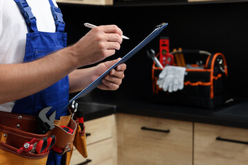 Professional plumber with clipboard and tool belt indoors, closeup. Space for text