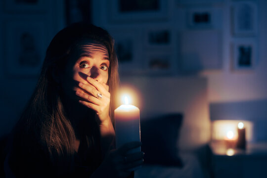 Stressed Woman Holding a Candle in Blackout No Power Situation. Unhappy person sitting in the dark at candlelight alone 
