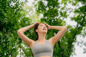 Naklejka na ściany i meble Asian woman trainer is engaged in fitness in public park. Female wearing sport bra and using headphone listening to music. Healthy lifestyle, sports outdoor activities in park