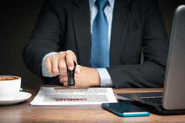 A businessman in a suit stamped for canceled documents while sitting at the table - obrazy, fototapety, plakaty