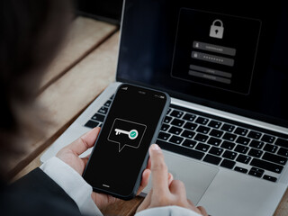 Two-factor authentication (2FA) concept. Key icon on smart phone screen in hand near laptop...