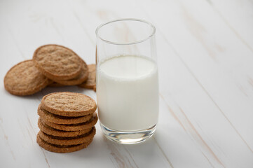 Oatmeal cookies and a glass of milk on a white wooden background.