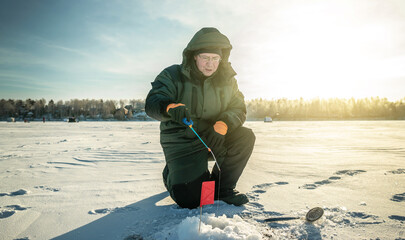 Fisherman is fishing in a hole on a large frozen lake on a sunny day. The joy of winter fishing