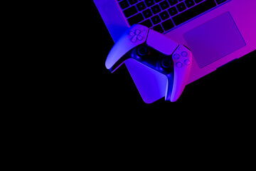 Modern white gamepad and laptop illuminated red and blue on a black background, copy space, top view.