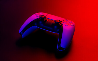 Modern white gamepad illuminated red and blue on a dark background, game controller for video games.