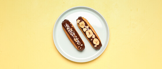 Plate with sweet eclairs on yellow background, top view