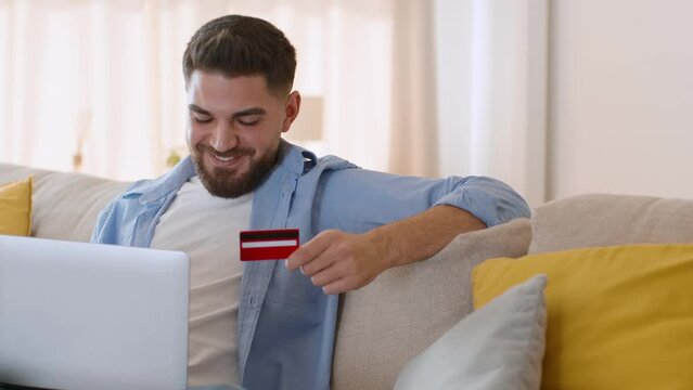 Young relaxed arab man shopping in internet, entering credit card data on website on laptop, tracking shot, empty space