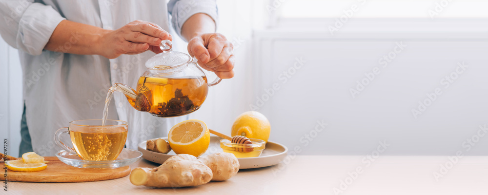 Wall mural women's hands pour hot drink ginger root tea lemon from teapot for cold treatment and prevention