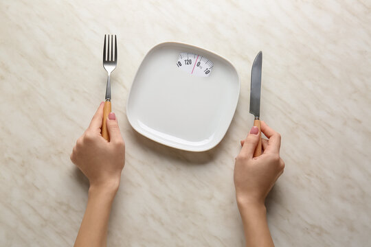 Female hands with empty plate and cutlery on light background. Diet concept