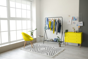 Rack with stylish clothes and yellow furniture in dressing room