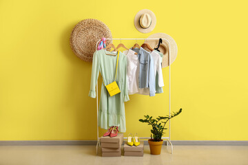 Rack with stylish clothes and accessories near yellow wall