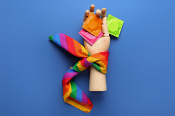 Wooden hand with condoms and rainbow scarf on blue background. Sex concept