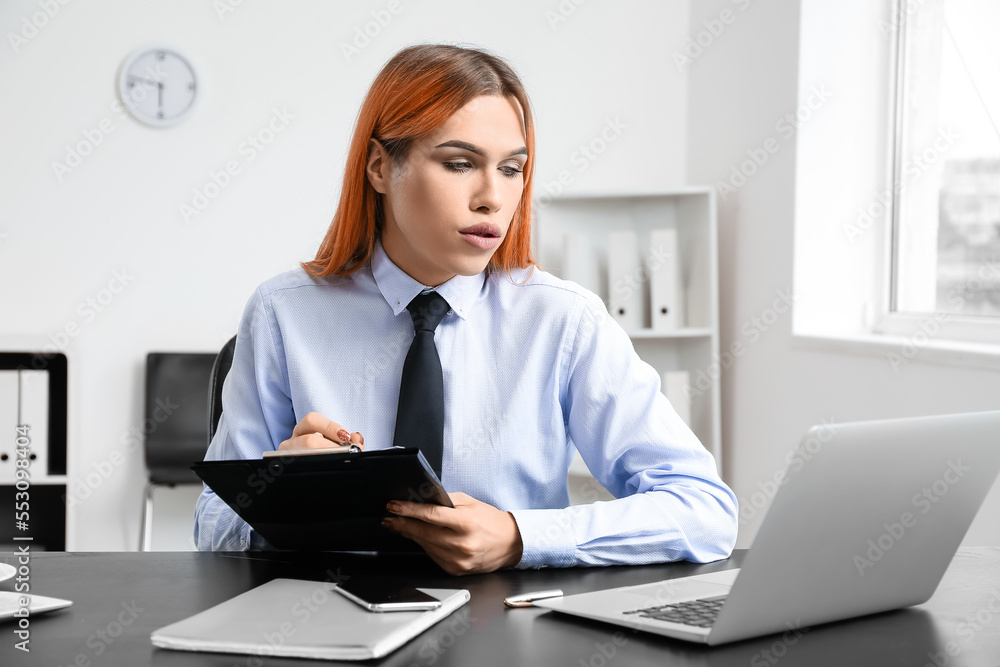 Poster beautiful transgender secretary working with clipboard and laptop at table in office