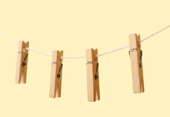Wooden clothespins hanging on rope against color background