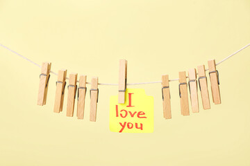 Wooden clothespins and sticky note with text I LOVE YOU hanging on rope against color background