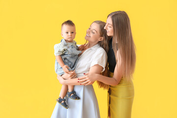 Happy lesbian couple with their little baby on yellow background