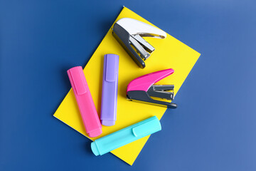 Notebook, staplers and markers on blue background