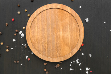 Wooden cutting board with peppercorns and sea salt on black background