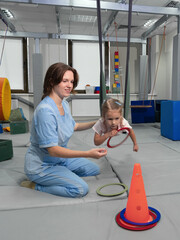 Child with physiotherapist on swing during sensory integration session. Little girl in...