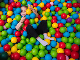 Cute little girl playing on multi coloured plastic balls in big dry paddling pool in playing centre. Having fun in playroom