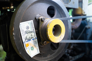 One hundred dollar banknote glued to a tractor pulley close-up - obrazy, fototapety, plakaty