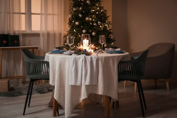 Christmas table setting with burning candles and fir branches in dining room