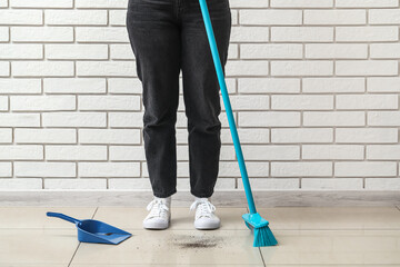 Woman with cleaning broom and dustpan near brick wall