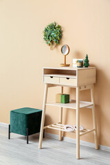 Table with mirror, presents, pouf and Christmas mistletoe wreath on beige wall
