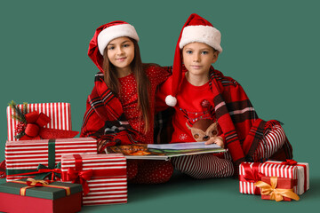 Little children in pajamas with Christmas gifts reading book on green background