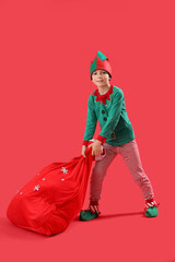 Little boy in elf pajamas with bag of Christmas gifts on red background