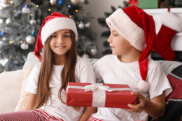 Little children in pajamas with Christmas gift sitting at home