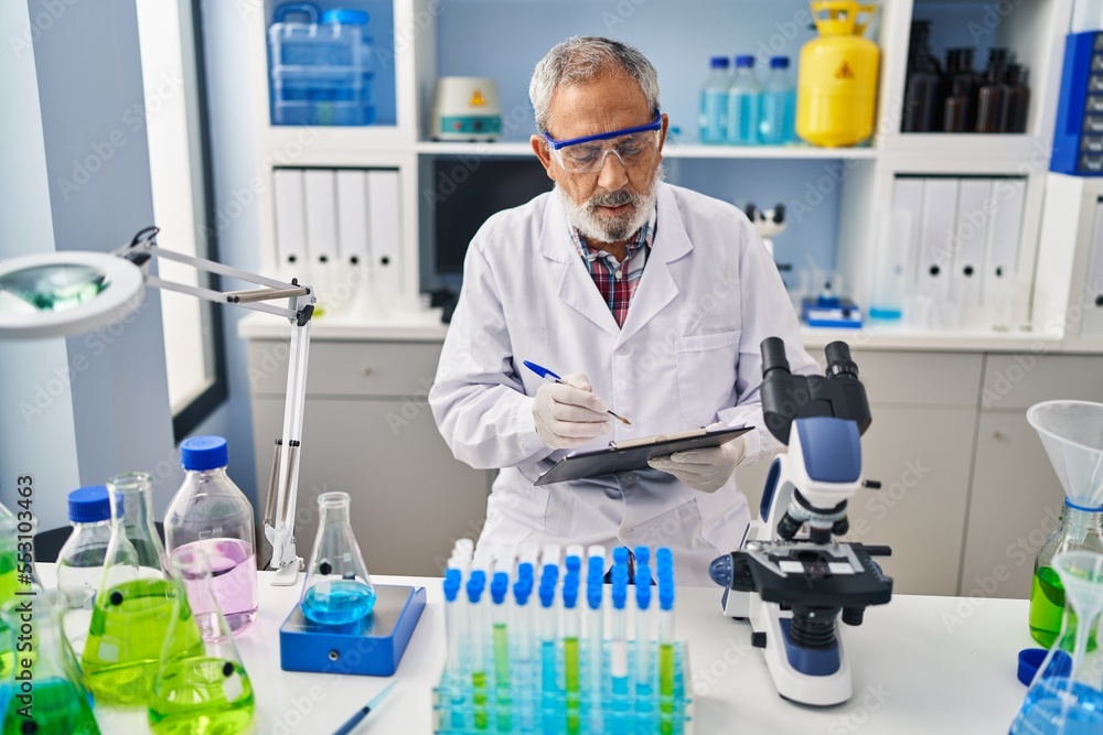 Wall mural Senior grey-haired man scientist writing report working at laboratory