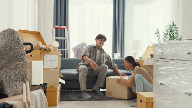 Young Asian couple help each other moving carton box full of stuff get some rest sit on sofa couch in living room at new house. Husband and wife move new house, Apartment Rent And Ownership Concept.