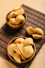 Bamboo mat with bowls of fortune cookies on beige background, closeup