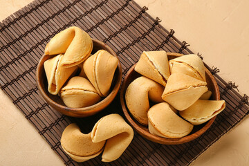 Bamboo mat with bowls of fortune cookies on beige background, closeup