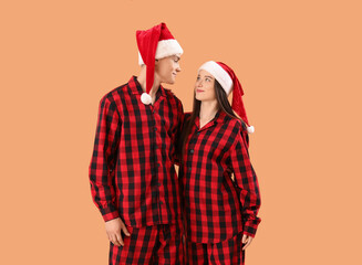 Young couple in Santa hats and pajamas on beige background