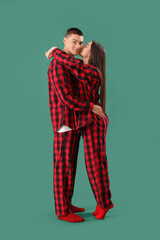 Young couple in checkered pajamas hugging on green background