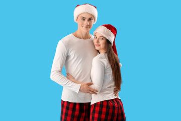 Obraz premium Young couple in Santa hats hugging on blue background