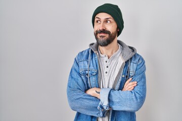 Young hispanic man with tattoos wearing wool cap smiling looking to the side and staring away thinking.