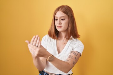 Young redhead woman standing over yellow background suffering pain on hands and fingers, arthritis...