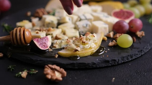 Woman pours crushed walnut onto Sliced Traditional Italian Gorgonzola cheese on stone seving board