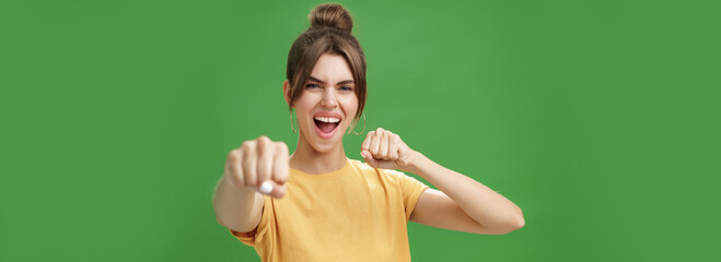 Cute female rebel in yellow t-shirt with gap teeth pulling fist towards camera as if showing...