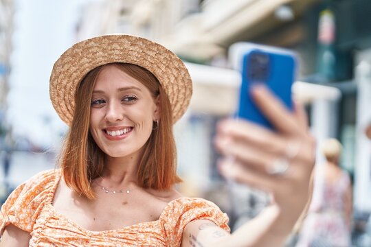 Young redhead woman tourist wearing summer hat make selfie by smartphone at street
